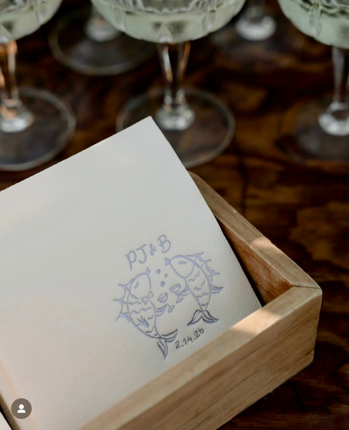 Custom foil printed white napkins with dusty blue and print. The design features to fish cheering with champagne coupe glasses and includes personalized initials and wedding date