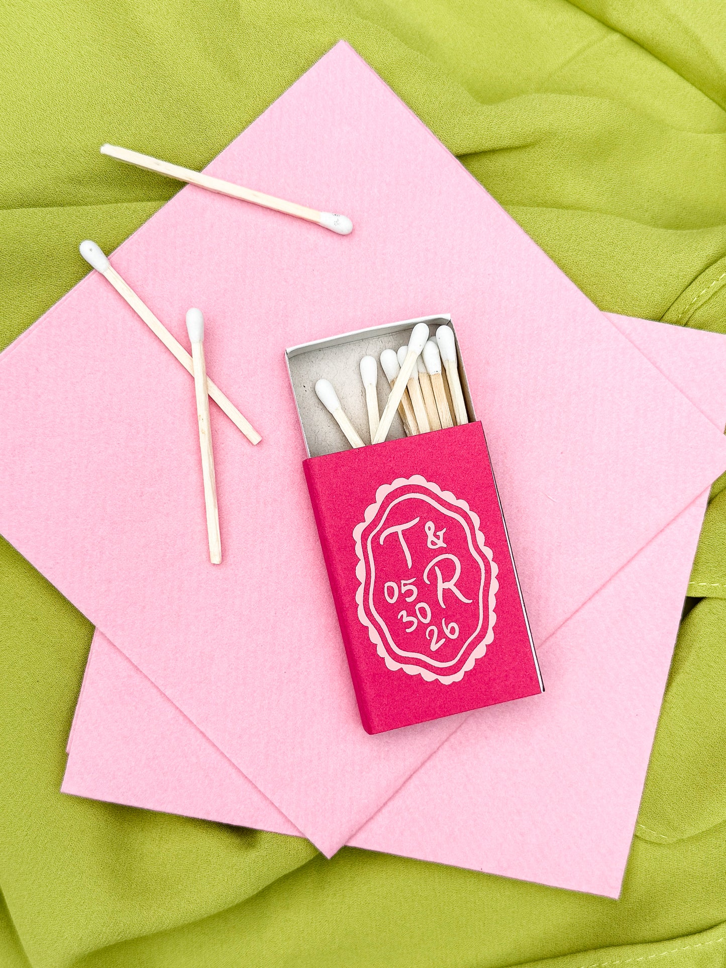 Custom printed hot pink matchbox with personalized initials and date on a background of pastel pink napkins and chartreuse tablecloth