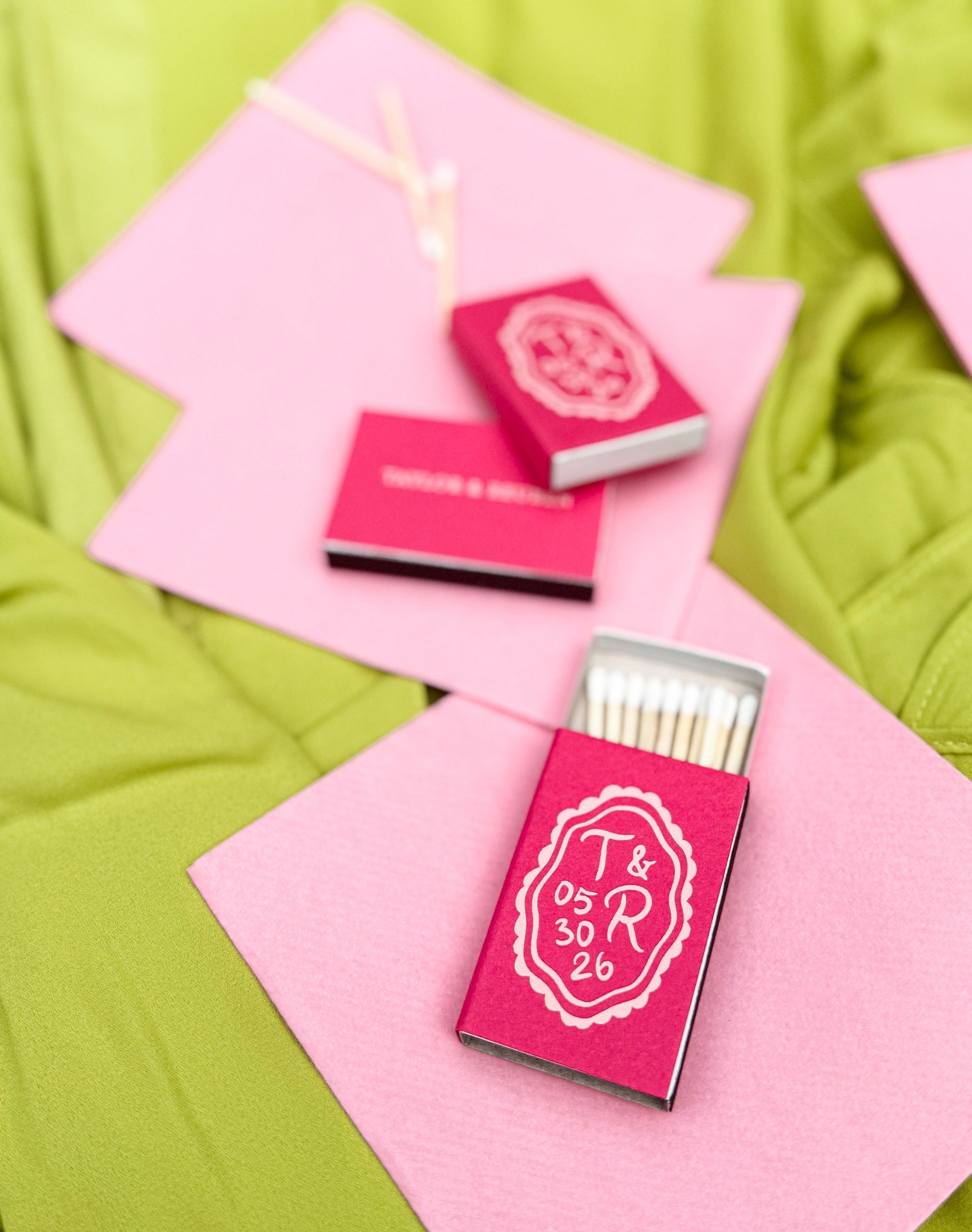 Custom foil printed hot pink matchboxes with white text on a chartreuse fabric background